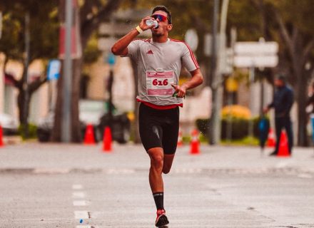 A dedicated runner drinks from a water bottle during a marathon on a city street.