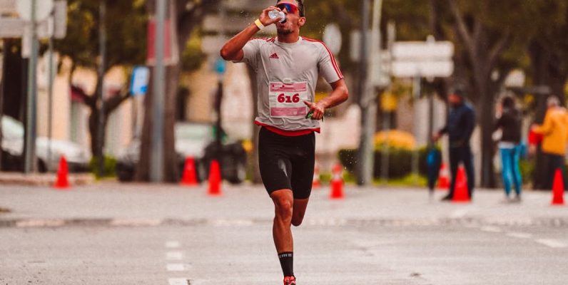 A dedicated runner drinks from a water bottle during a marathon on a city street.