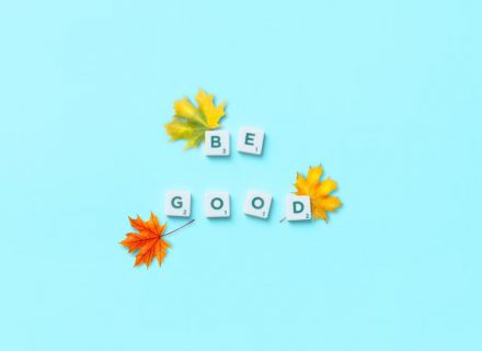Top view of 'Be Good' phrase with maple leaves on blue background, inspiring mindfulness.