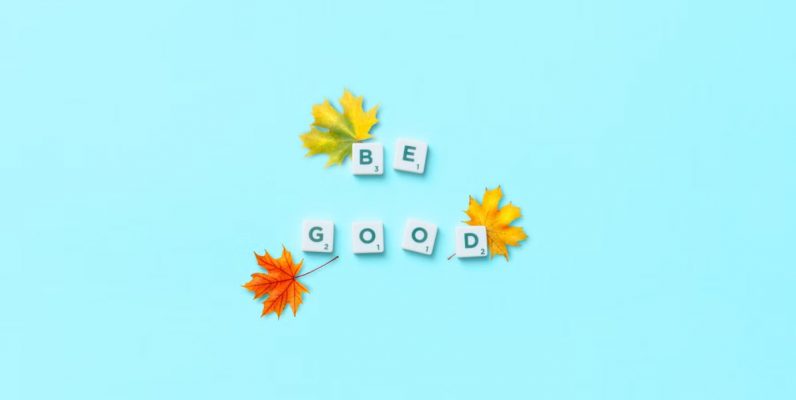 Top view of 'Be Good' phrase with maple leaves on blue background, inspiring mindfulness.